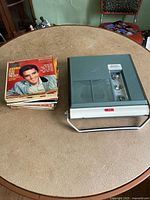 Photo showing the portable record player next to a stack of vintage 45 RPM records with Elvis Presley on the top album.
