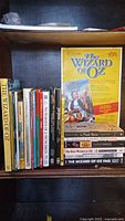 Photo showing 22 Wizard of Oz books lined up on a shelf plus a Wizard of Oz poster displayed on the right side.