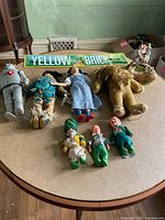 Wide shot showing all items including Tin Man, Cowardly Lion, Dorothy, three Munchkin dolls, Yellow Brick Road metal sign, and Wizard of Oz statuette.
