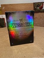 Front view of the holographic Wrestlemania Anthology DVD box set standing upright on a textured surface.