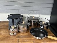 Full view of the 10-piece camping cooking set including pots with lids and frying pan, displayed on a wooden surface