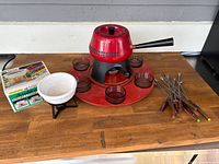 Overall view of the red fondue set with glass bowls, forks, and the chocolate fondue set boxed with ceramic pot and stand.