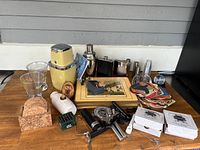 Wide shot of overall lot showing all items including cocktail shakers, glass tumblers, cork coasters, ceramic flask, metal flasks, bar tools and paper mats.