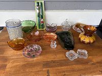Overview of all carnival glassware and decorative glass items on a wooden tabletop, various colored bowls, dishes, and vases visible.