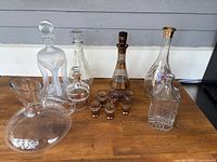 All items arranged on wood surface: four decanters, six small glasses, one glass pitcher.