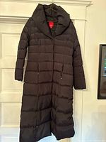 Front view of long black puffer coat with quilted horizontal lines and large collar hanging on a hanger.
