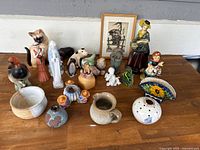 Photo of assorted ceramic and pottery figurines and vessels arranged on wooden surface.