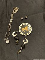 Lot of sterling silver jewelry including necklace, stud earrings, dangle earrings, and pin displayed on black background.