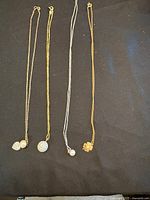 Four necklaces laid out on black fabric. Visible pendants include pearl, crystal heart, flower, and spherical crystals.