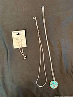 Sterling silver dangle earrings on card and two sterling silver necklaces laid out on dark background showing pendants and chain styles.