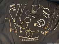 A top view photo showing various jewelry items including necklaces, bracelets, bangles, and pendants arranged on black fabric