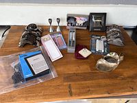 Display of whole lot including Kindle, masks, candlesticks, calculator, writing pad, electronic accessories, and silver-tone kitchenware on a wooden table