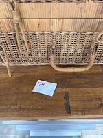 Close-up of one wicker picnic basket handle and latch closure on wooden table.