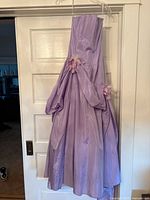 Full view of purple formal dress hanging on door, showing gathered skirt and floral fabric accents on hips.