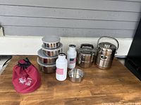 Full set of assorted stainless steel kitchenware including bowls, bottles, tiffin boxes, small bowl, and red storage bag.