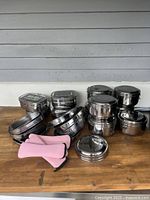 Overview of all stainless steel containers and pink oven mitts displayed on a wood surface.