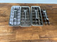 Four stainless steel ice cube trays arranged horizontally on wooden surface with lever mechanisms visible.
