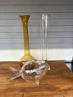 Two tall glass vases and one large clear decorative glass fish on wooden surface