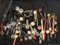 Full lot of 25 wristwatches and pocket watches laid out on black background showing various styles, colors, and band types.