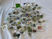 Wide view of about 50 assorted McDonald's collectible pins individually bagged on white cloth surface, showing variety of colors and designs in mixed themes including Coca-Cola, Olympics, and Disney.