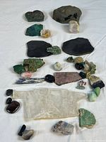 Overview of mixed mineral and gemstone collection arranged on white cloth showing various colors and sizes from small tumbled stones to larger rough specimens.
