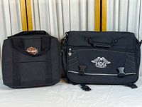 Two black bags side by side: a compact lunch bag with Harley-Davidson shield logo and larger HOG messenger bag with front flap and clip closures.