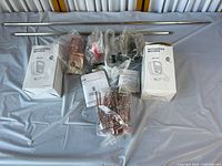 Two boxed rotisserie motors, multiple stainless steel rods of 2.5 inches and 31.5 inches length, and several sealed bags containing rotisserie mounting components arranged on a sheet.