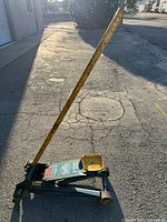Full view of the Lincoln mechanical floor jack showing its blue and yellow painted metal body with attached long yellow handle and wheels on concrete ground.