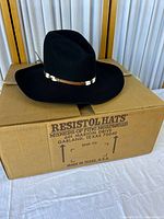 Black Resistol hat displayed on top of its original hat box with printed details showing the brand and manufacturing location in Garland, Texas, USA.