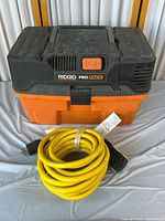 Ridgid Pro Pack wet/dry vacuum cleaner with accessory case and yellow extension cord in front.