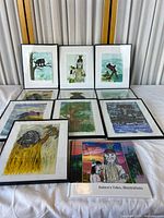 Overview of 8 framed prints arranged on a table, showing various native and folk art subjects, animals, and nature in mixed media with black frames
