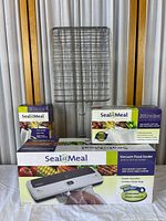 Seal-a-Meal vacuum food sealer and packaging boxes for storage bags and rolls displayed in front of a metal display grid.