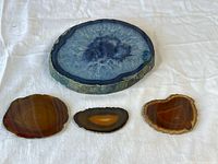 Four polished agate geode slices shown on white cloth including one large blue slice and three smaller brown and amber slices.