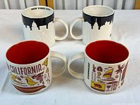 Two Starbucks ceramic mugs side by side: one with New York City skyline in black and white, one with California symbols in colorful print red inside.