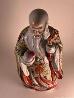 Front view of the porcelain figure depicting an immortal man holding a peach and staff, detailed Famille Rose decoration.
