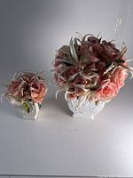 Pair of two artificial flower arrangements featuring pink roses and white lilies in white ceramic vases with embossed floral patterns, shown on white background.