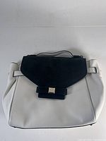 Front and full view showing white pebbled leather body and black faux croc flap with bow detail and clasp.