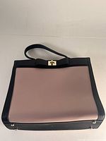 Full front view of dusty pink handbag with black trim and gold hardware with bow detail, flat on surface.