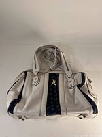 Front view of white leather satchel bag with black velour vertical stripes, gold-tone 'L' detail plaque, dual handle straps.