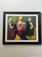 Front view of framed serigraph showing three musicians playing string instruments in vibrant colors with artist signature and numbering visible in bottom margin.
