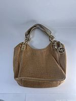 Front view of the Michael Kors woven straw handbag with gold hardware, showing the MK logo charm on the handle.