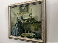 Framed artwork depicting a man playing piano and a woman standing beside in an elegant room.