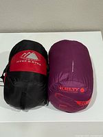 Photo of two rolled backpacking sleeping bags: Hyke & Byke black and red, and Kelty Cosmicdown purple with temperature rating visible