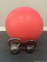 Two kettlebells (26 and 15 lbs) in front of a red Bodyfit exercise ball on black diamond-pattern flooring.