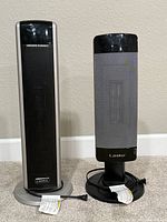 Two Lasko tower space heaters side by side on floor showing front.