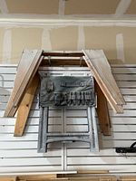 Front and top view of two collapsible metal saw horses with attached canvas tool pouches and two wooden standard saw horses stacked behind.