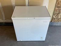 Front side view of white Insignia chest freezer showing dents on front bottom panel and thermostat.