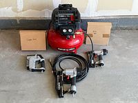 Full lot: red Porter Cable compressor on floor, two labeled boxes behind, three pneumatic tools in front