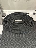 Full view of coiled black twisted battle rope on textured rubber flooring
