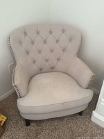 Front angle view of light beige upholstered accent chair with button-tufted back and cushioned seat showing slight staining.